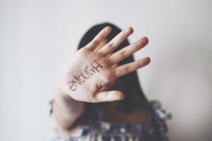 A woman with her palm covering her face but facing the camera with "enough" written on her hand