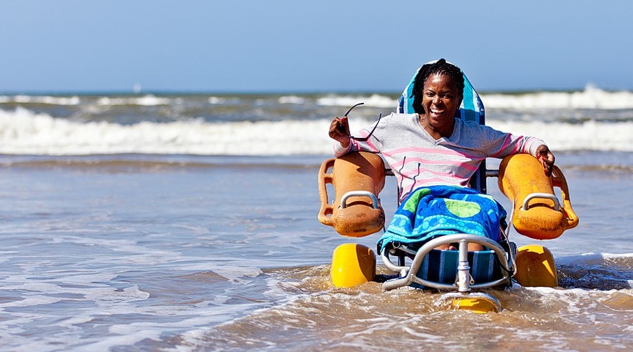 A smiling lady in a beach wheelchair has fun in the shallows at the beach